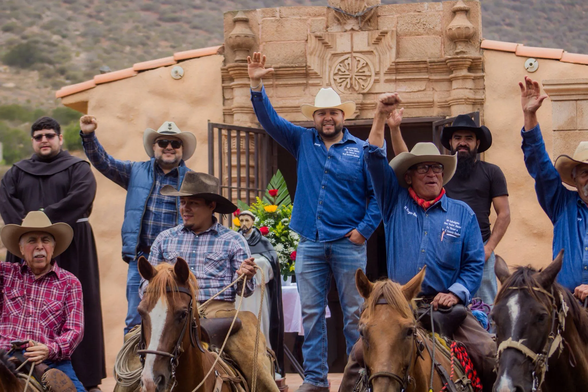 Personas a caballo y a pie levantando los brazos en forma de celebración en San Quintín, Una cabalgata grupal en La Ruta Vaquera, Baja California