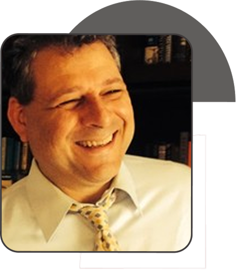 Smiling middle-aged man wearing a white shirt and patterned tie in front of a bookshelf.