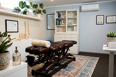Chiropractor treatment room with dark brown adjustment table, white cabinet, and plants on shelves.