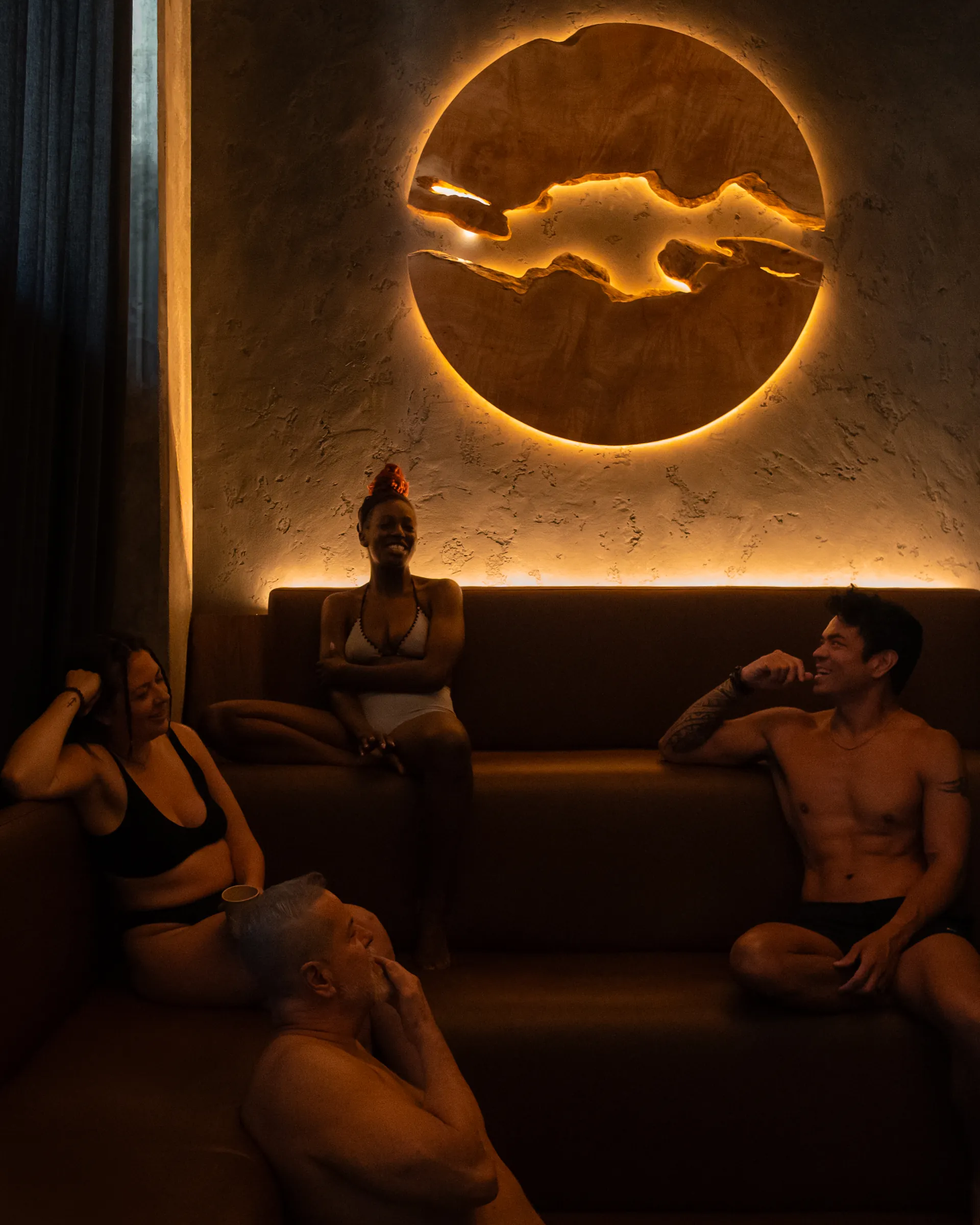 Friends unwinding during sauna experience at Aetherhaus Vancouver, sitting in a wellness lounge with warm ambient design.