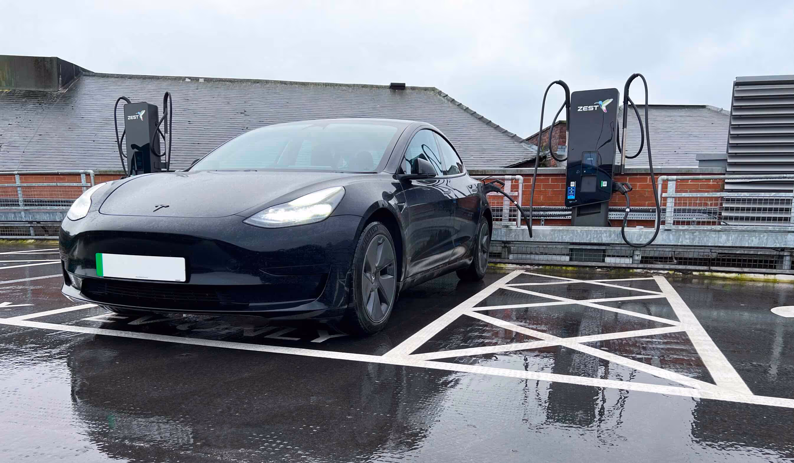 Black car charging using Zest charger in the rain in multi story car park