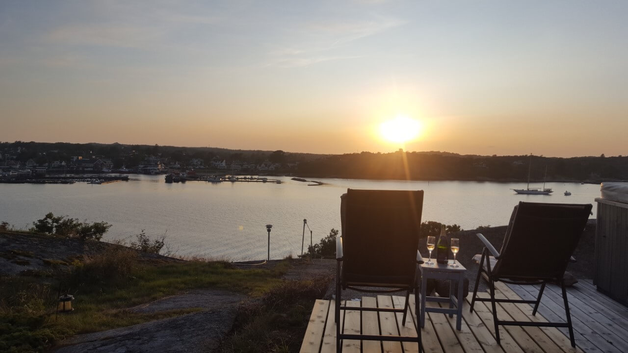 Solnedgang over åsene og havet sett fra terrassen med et par stoler på Gunnar Eckbos hytte Sandø ved Hvasser