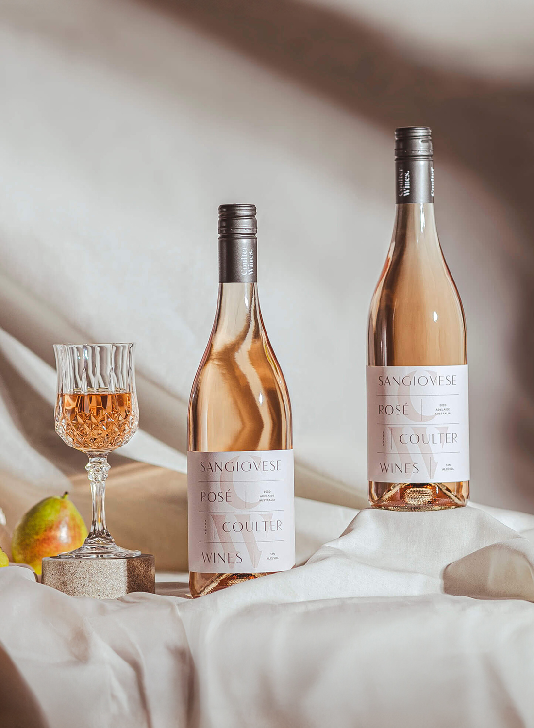 Wine bottle with glasses and fruit in soft, natural light.