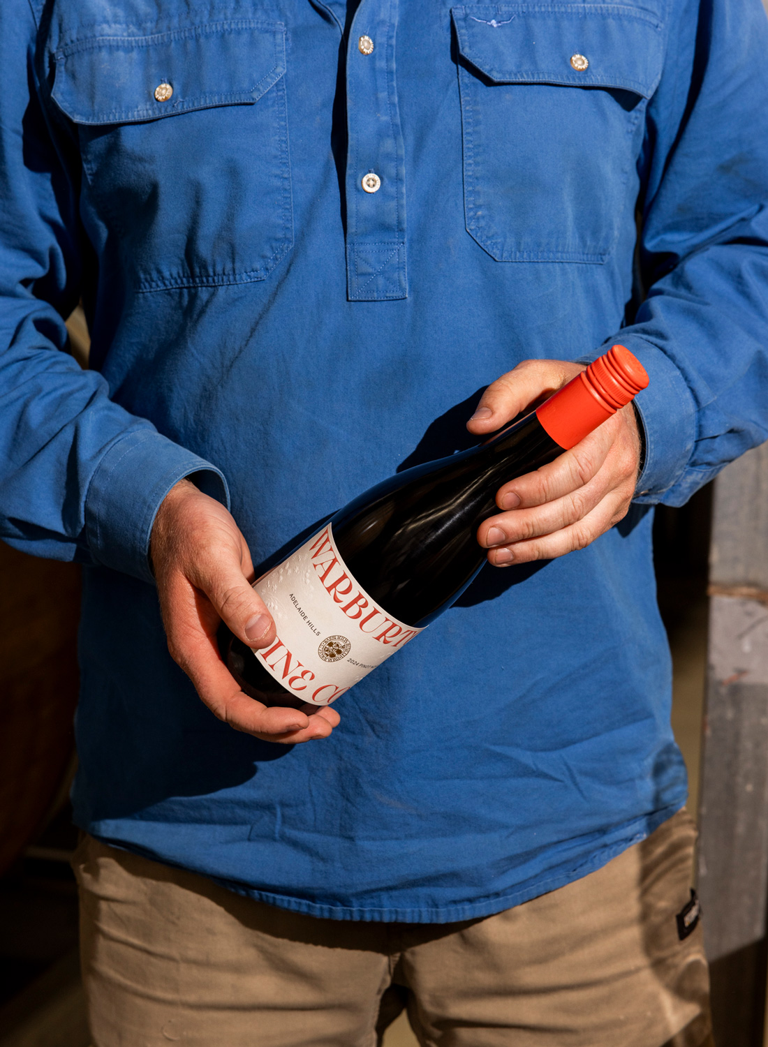 Man holding a wine bottle in front of chest.