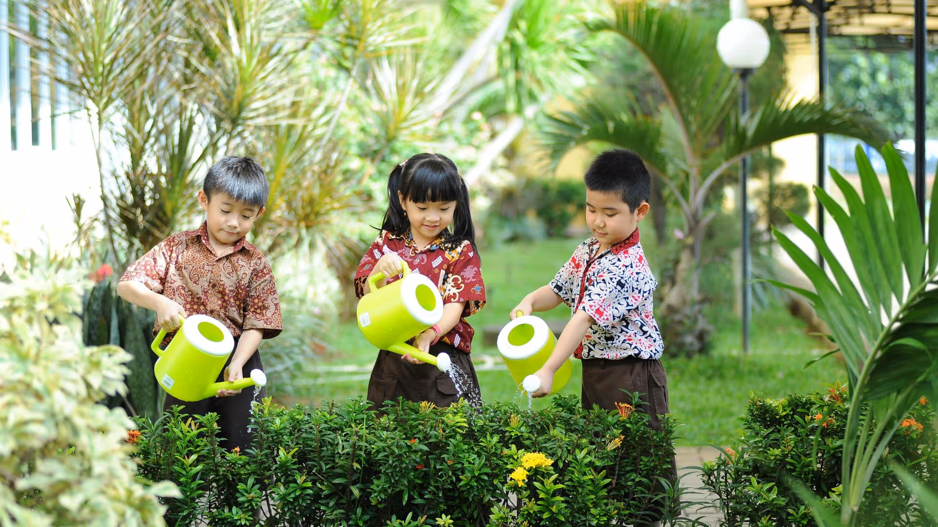 Three children are watering plants in a garden.