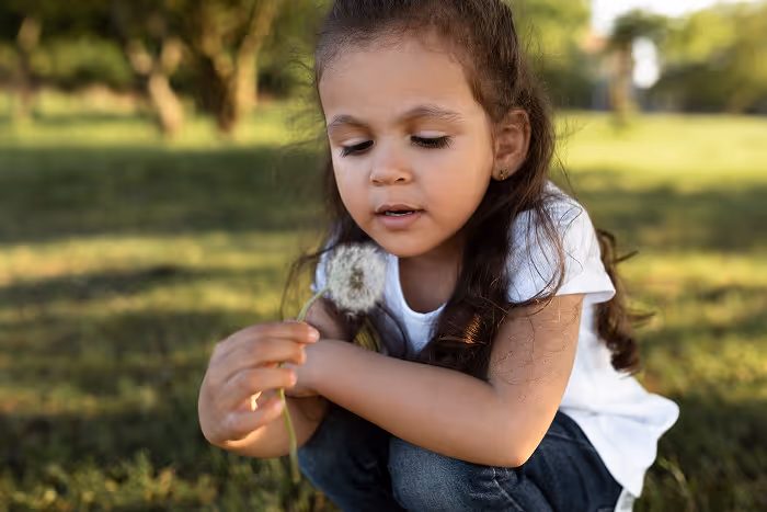 A little girl sitting in the grass holding a dandelion.