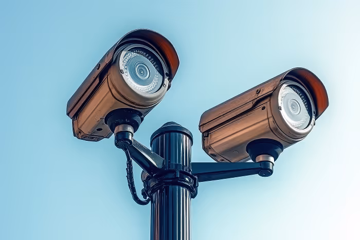 Two security cameras on a pole against a blue sky.
