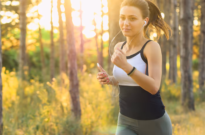 A woman running through a forest with trees in the background.