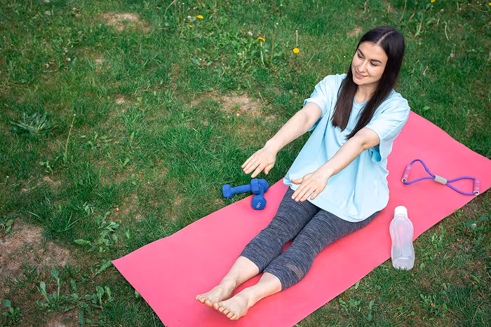 A woman sitting on a pink mat with a bottle of water.