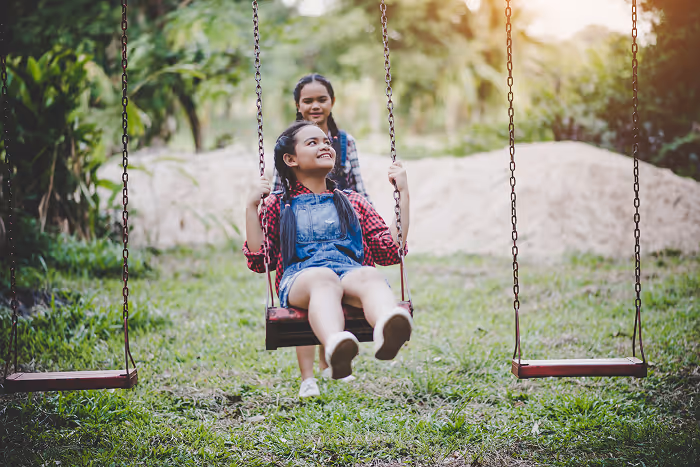 A woman sitting on a swing next to a little girl.