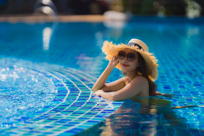 A little girl wearing a straw hat and sunglasses in a pool.