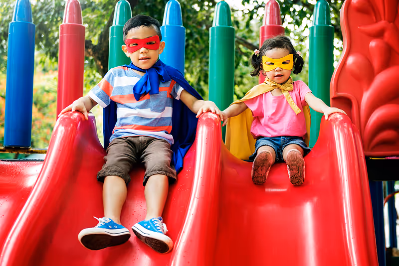 A couple of kids sitting on top of a red slide.