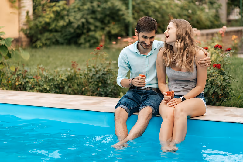 A man and a woman sitting on the edge of a swimming pool.