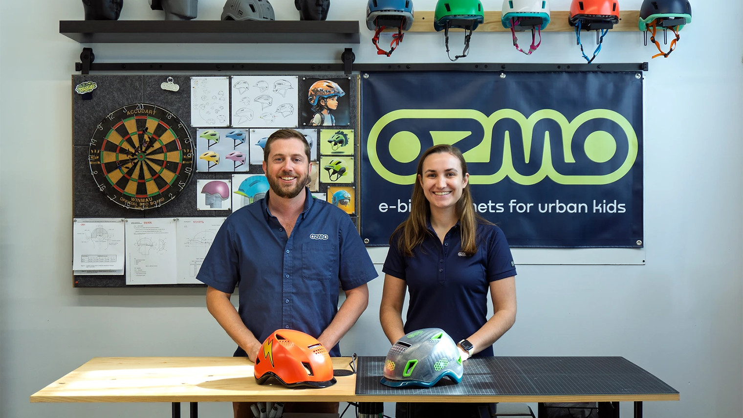 Ozmo team members standing in a design studio with kids bike helmets and branded workspace.