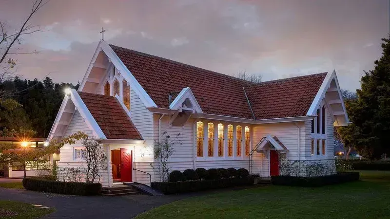 Alt text: "Exterior view of a charming white chapel with stained glass windows and a red door, set against a twilight sky. This serene building is part of St. Peter's School, offering a peaceful space for reflection and community gatherings on campus."