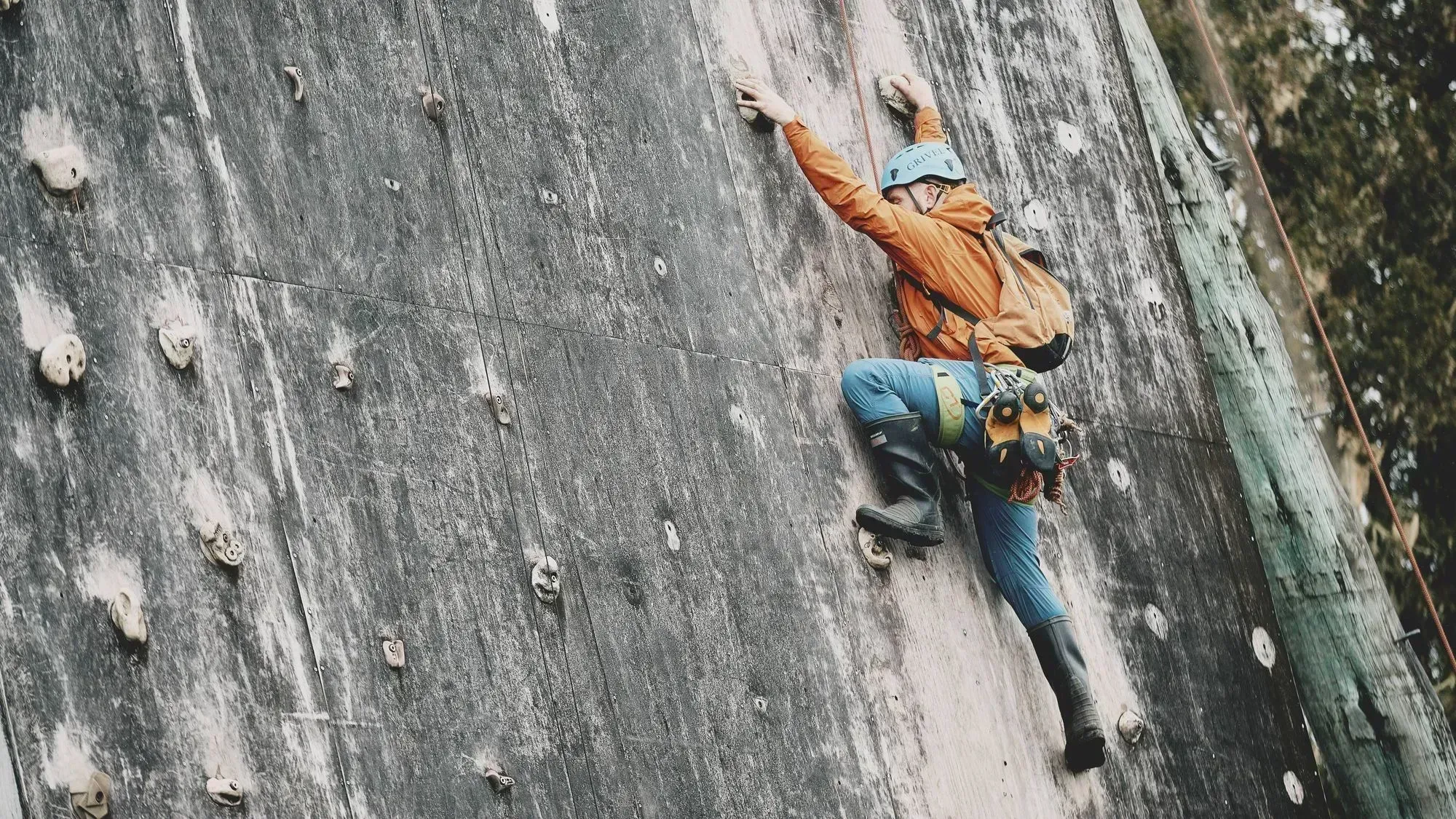 A climber in orange and blue gear ascends a challenging outdoor rock climbing wall, showcasing the vibrant sports programmes at St. Peter's School. This image highlights the school's commitment to fostering adventure and teamwork in an inspiring environment.