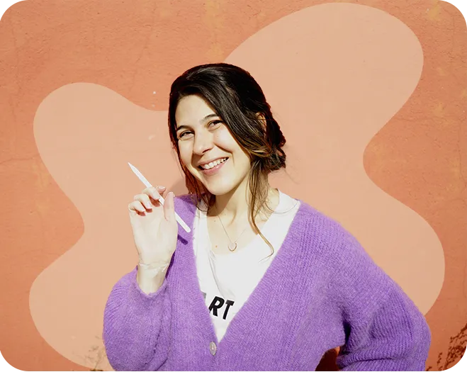 French Riviera based illustrator Patty Nigri smiling in a purple cardigan, holding a pencil