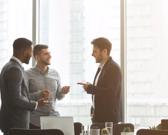 Three male collaborating in the office in formal work attires, with a large glass window in the background.