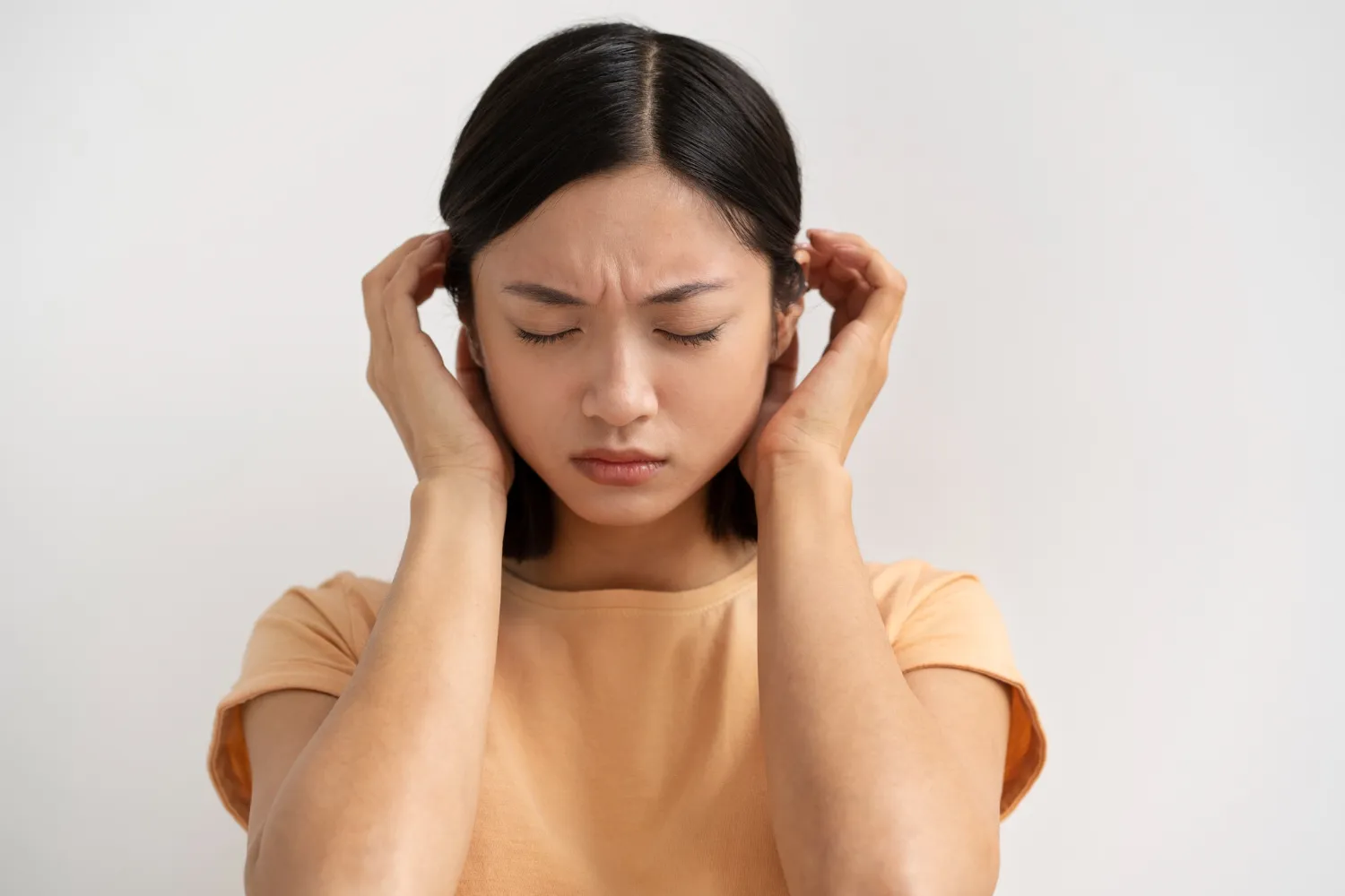 Young woman with eyes closed holding her ears, showing discomfort.