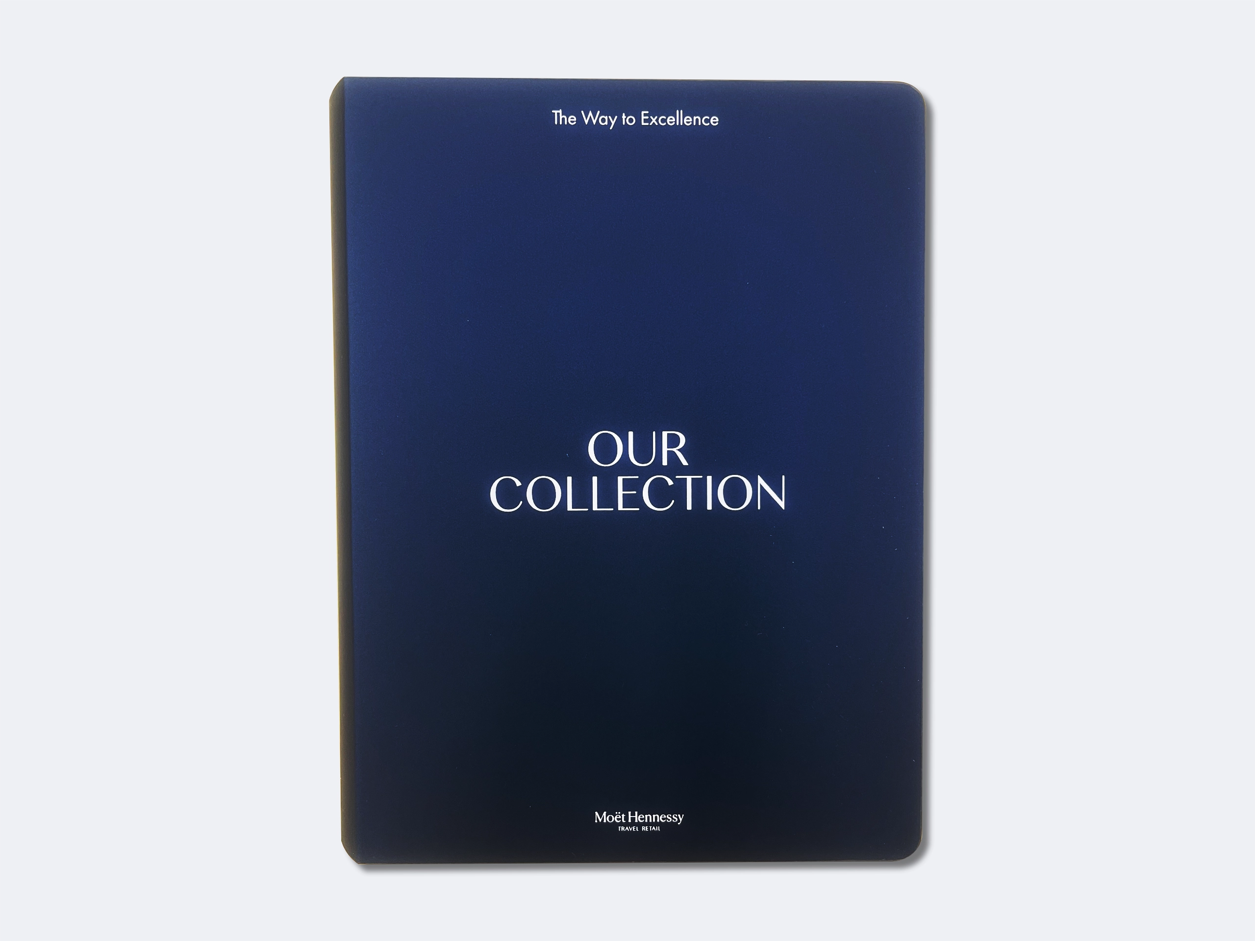 Blue book cover with white text reading 'The Way to Excellence' at the top, 'OUR COLLECTION' in the center, and 'Moët Hennessy TRAVEL RETAIL' at the bottom.