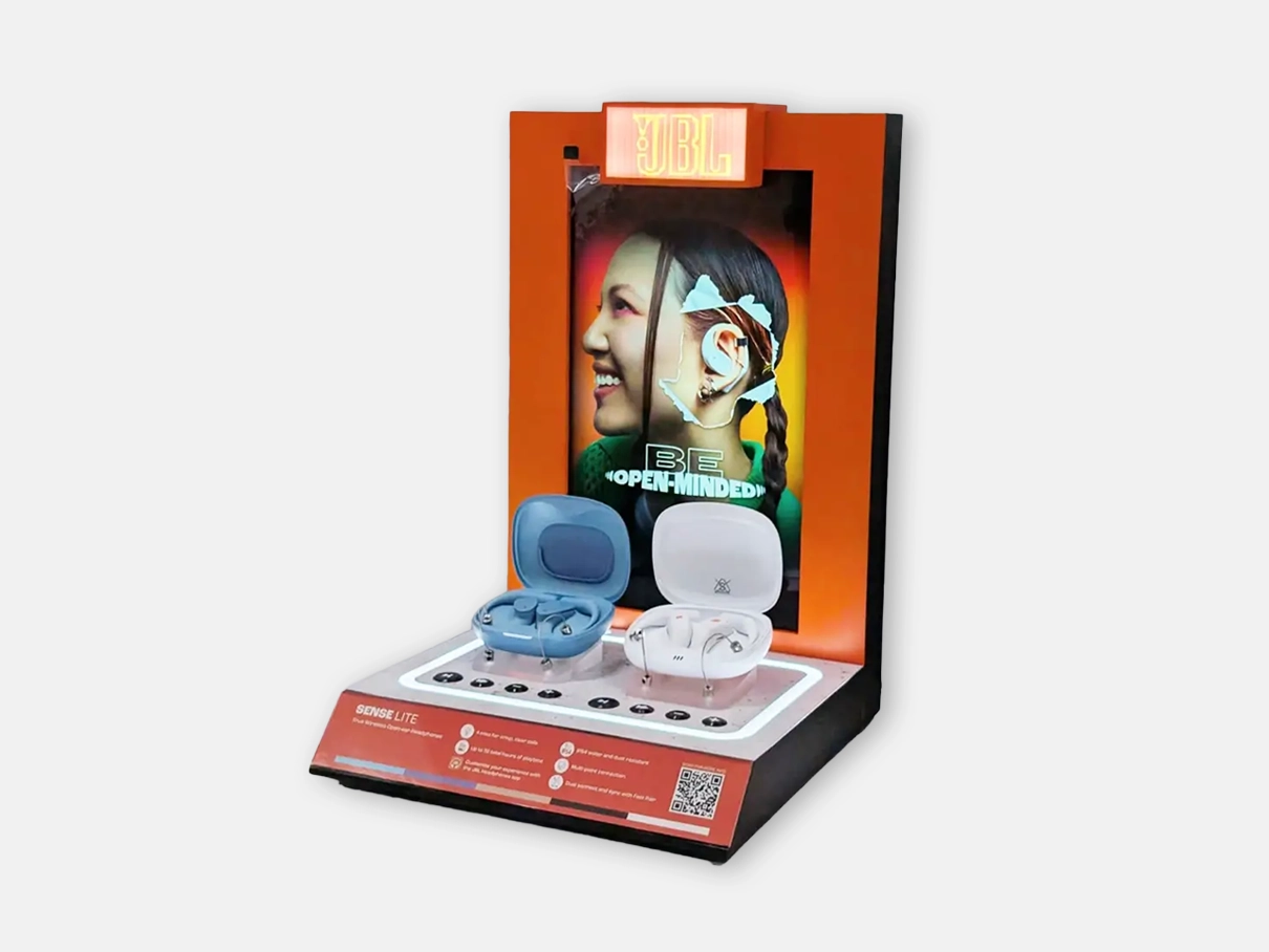 A vibrant POS display showcasing two pairs of wireless earbuds, set against a colorful backdrop featuring a smiling woman and the mottos 'BE OPEN-MINDED.' The display promotes JBL branding.