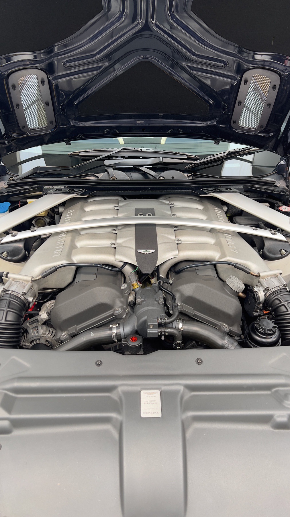 Engine bay of the Aston Martin DB9 showing the V12 engine and strut brace