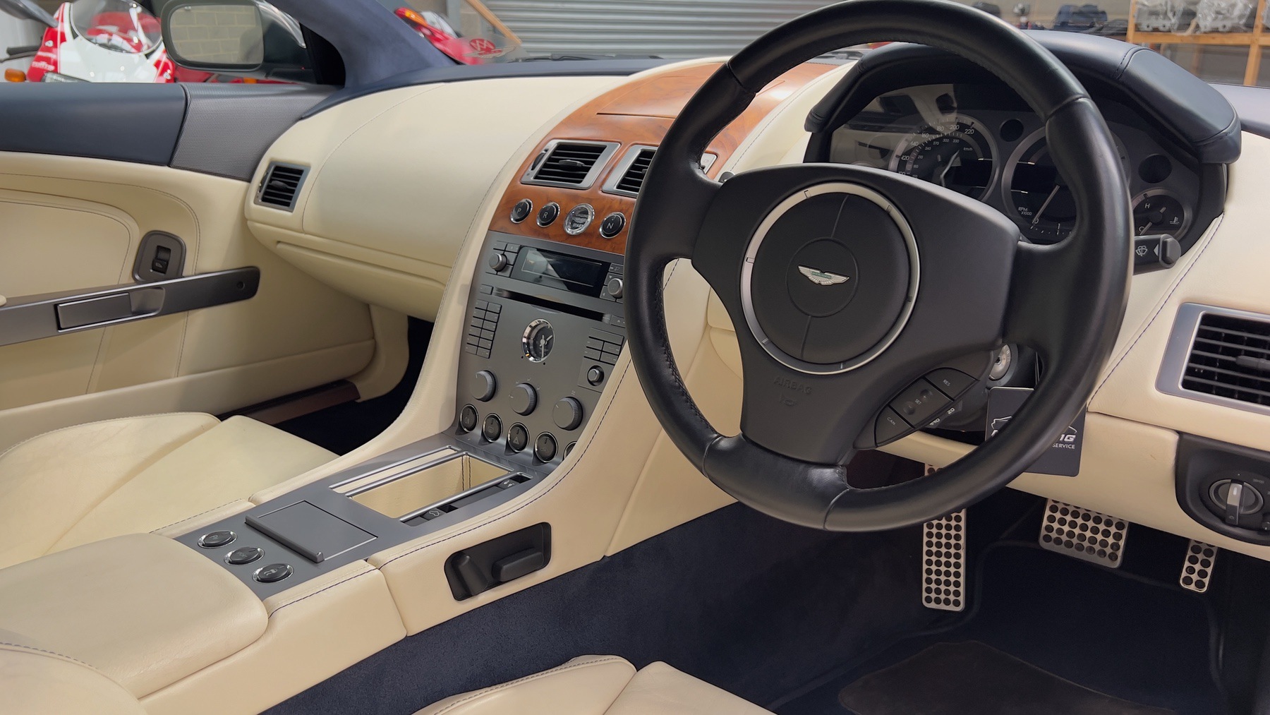 Driver's side of the Aston Martin DB9 cabin with steering wheel, walnut fascia and parchment leather