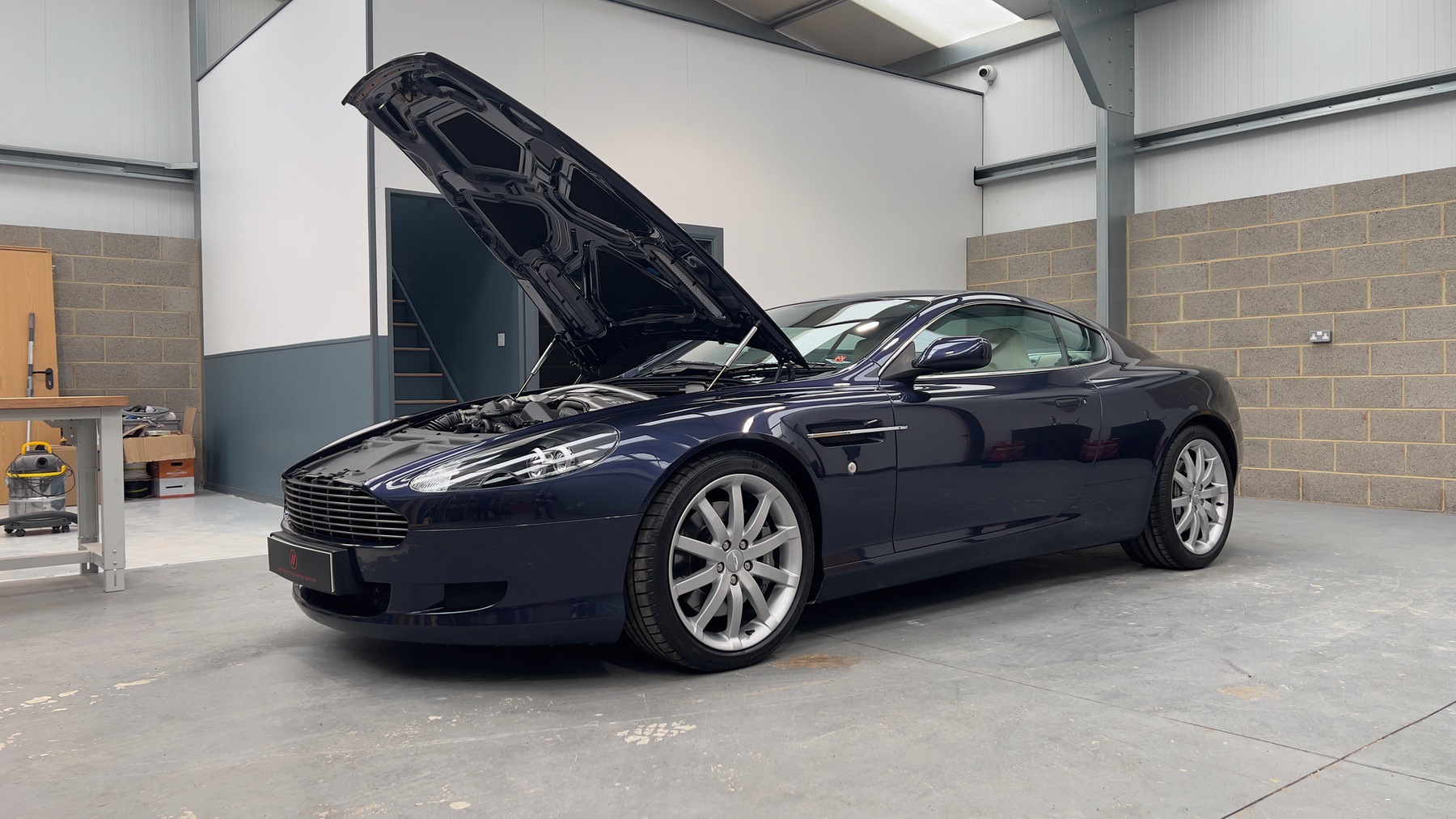 Aston Martin DB9 with its bonnet raised, showing the front three-quarter profile in Blue Sapphire Metallic
