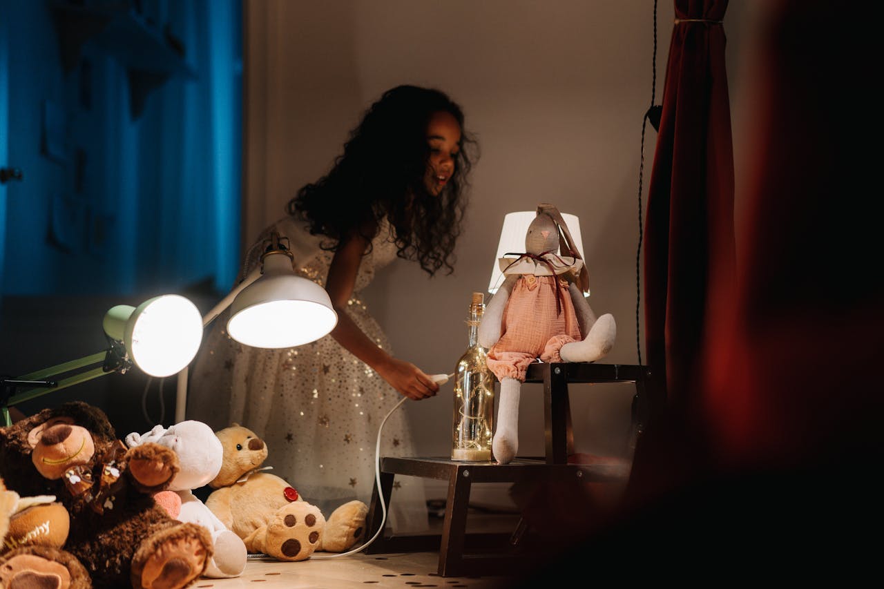 Une petite fille dans un endroittrès chaleureux. La lumière est tamisée et elle est entourée de nombreuses peluches