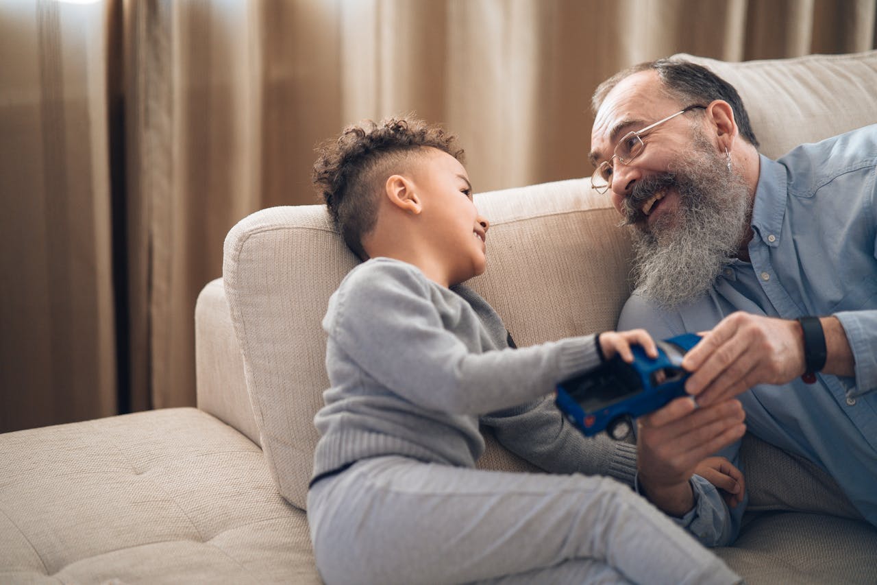 Un grand-père joue avec son petit fils sur un canapé. Ils se sourient
