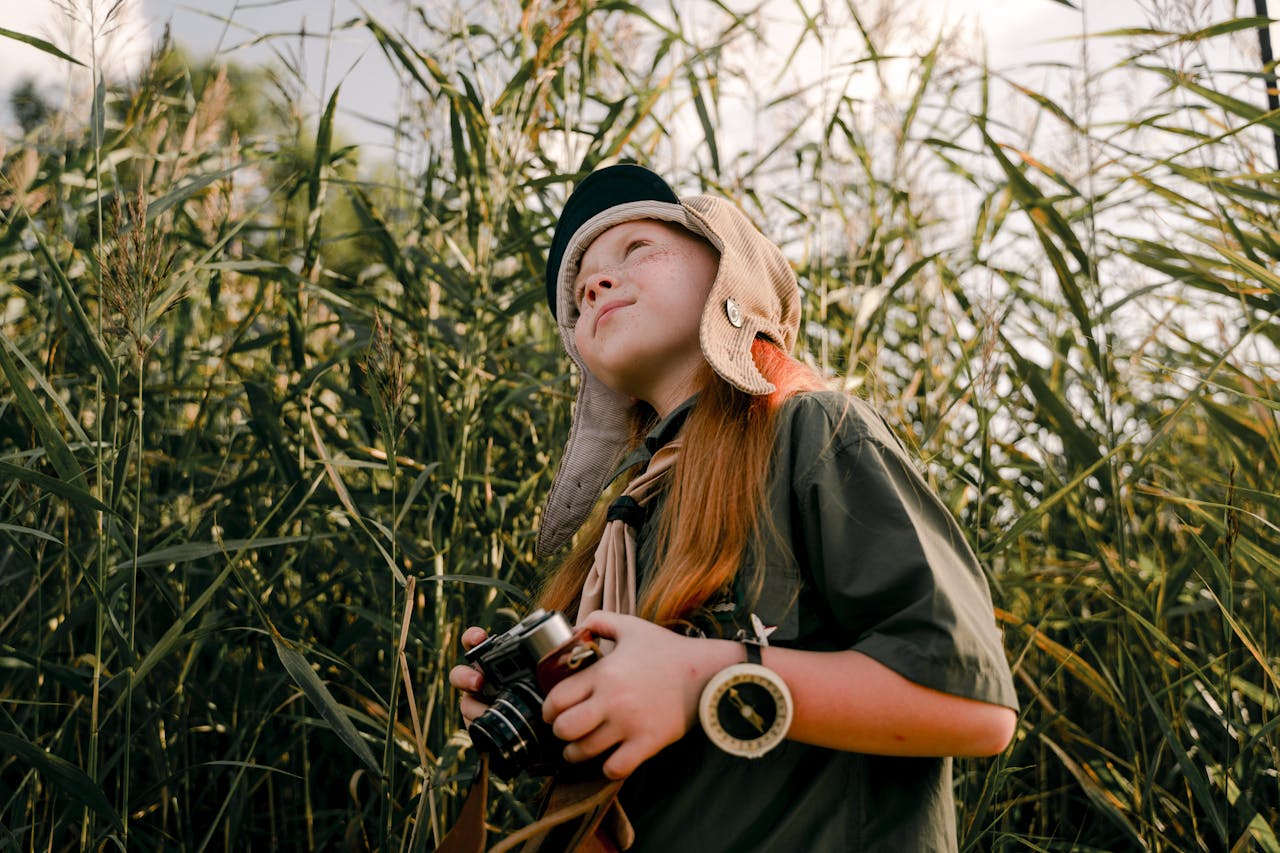 Une jeune fille se promne dans des herbes hautes avec un appareil photo à la main. Elle est en qûete d'aventure et de découverte