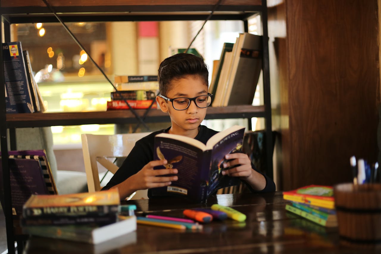 Un jeune garçon lit à la table d'une bibliothèque. Il est entouré de nombreux livres