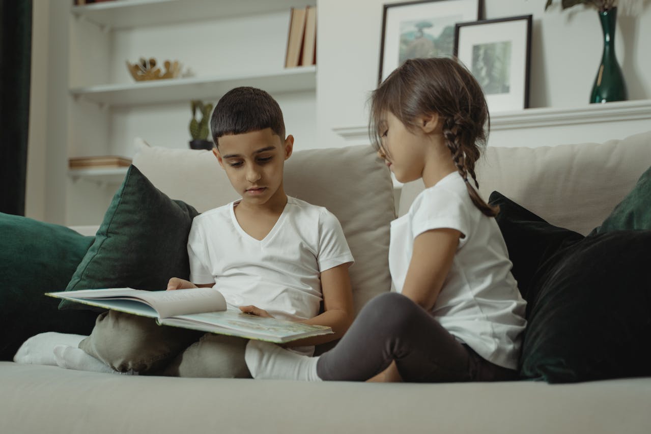 Deux jeunes enfants de 6 ans lisent un grand livre sur un canapé