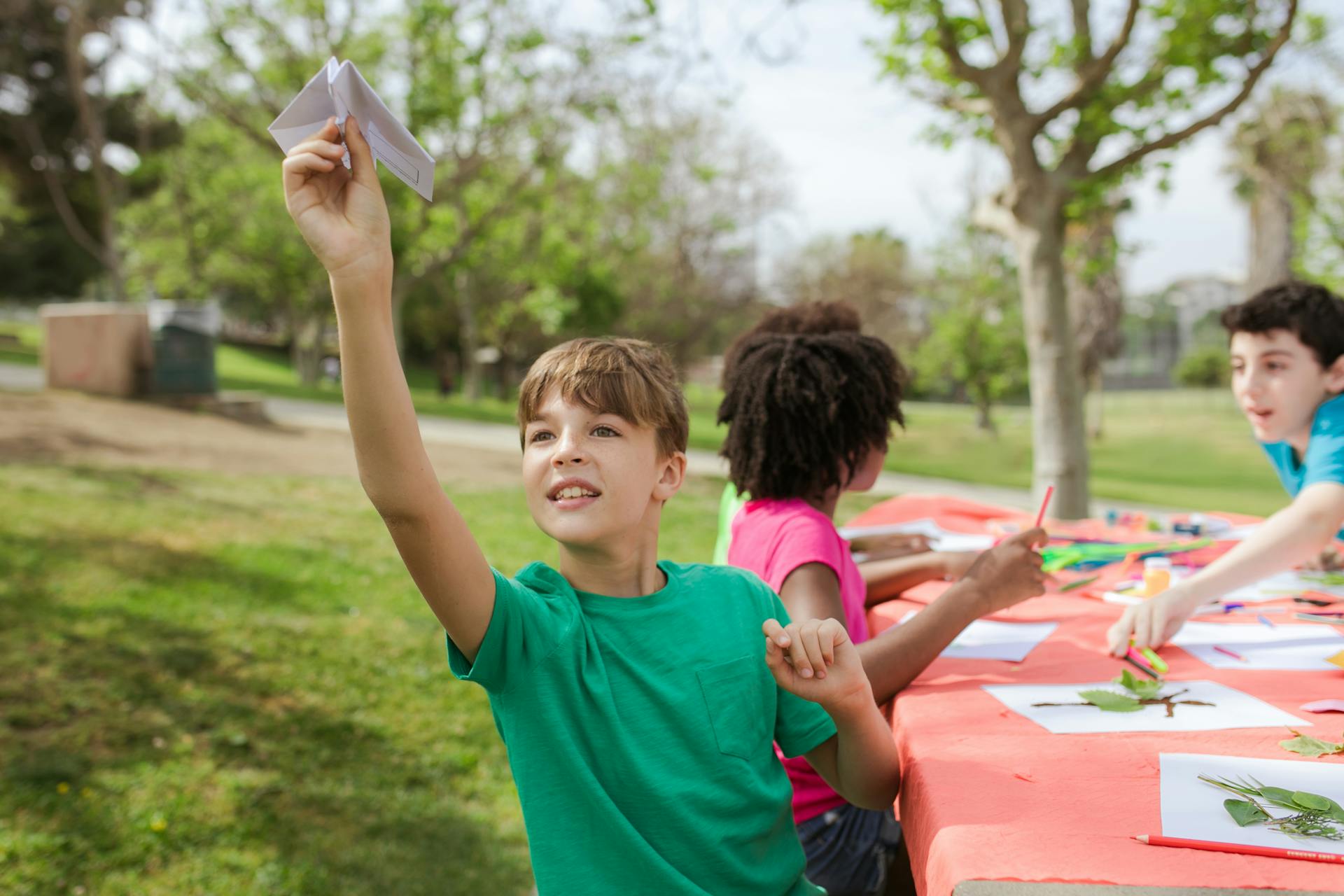 Des enfants jouent avec des feuilles sur une table de jardin, ils fabriquent un herbier