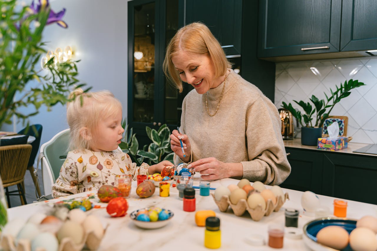 Une grand mère et sa petite fille peignent des oeufs dans leur cuisine