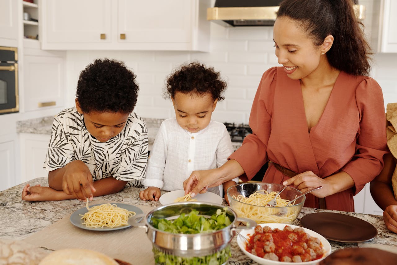 Une maman cuisine avec ses deux jeunes enfants. Ils partagent un bon moment de complicité