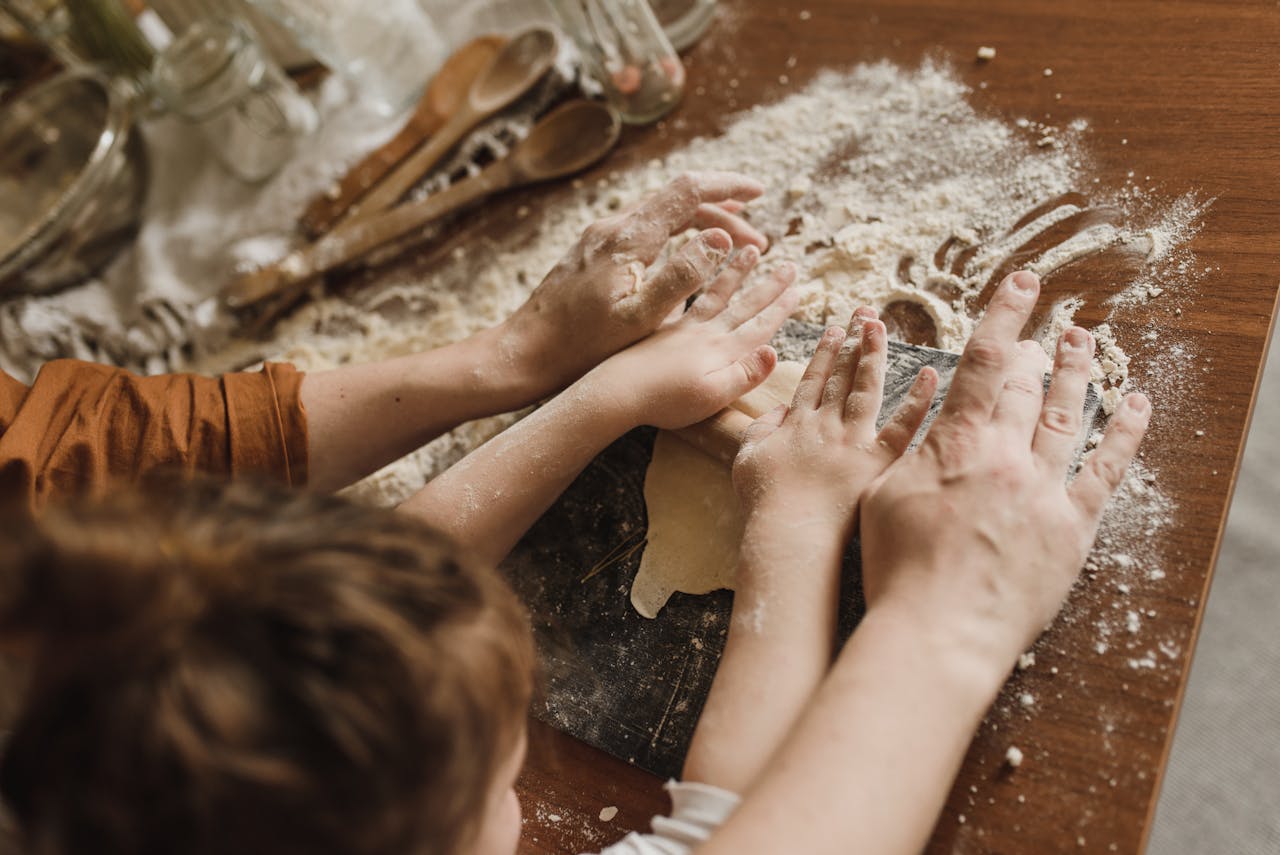 Un adulte aide un jeune garçon à étaler une pâte à pizza