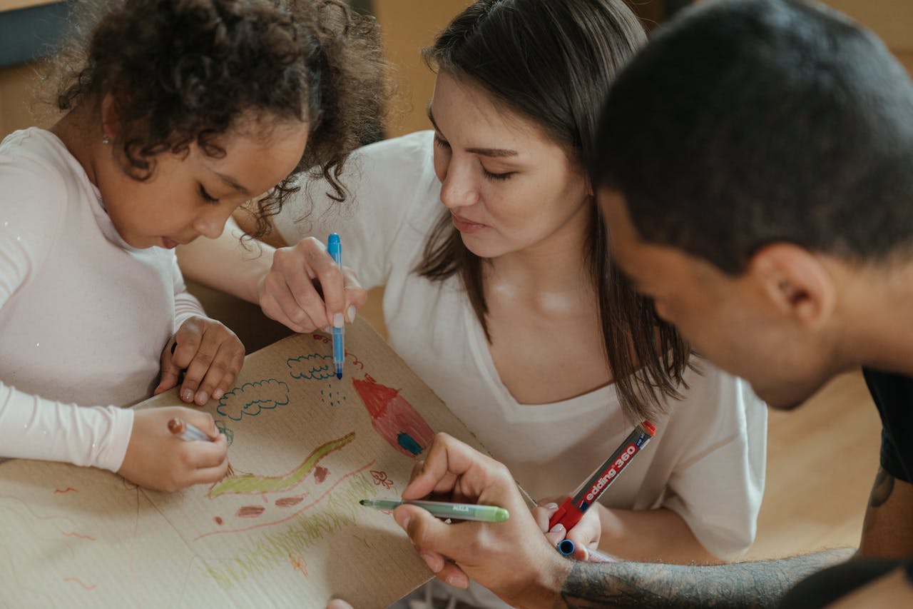 Des parents et leur jeune fille dessinant avec des feutres sur un carton