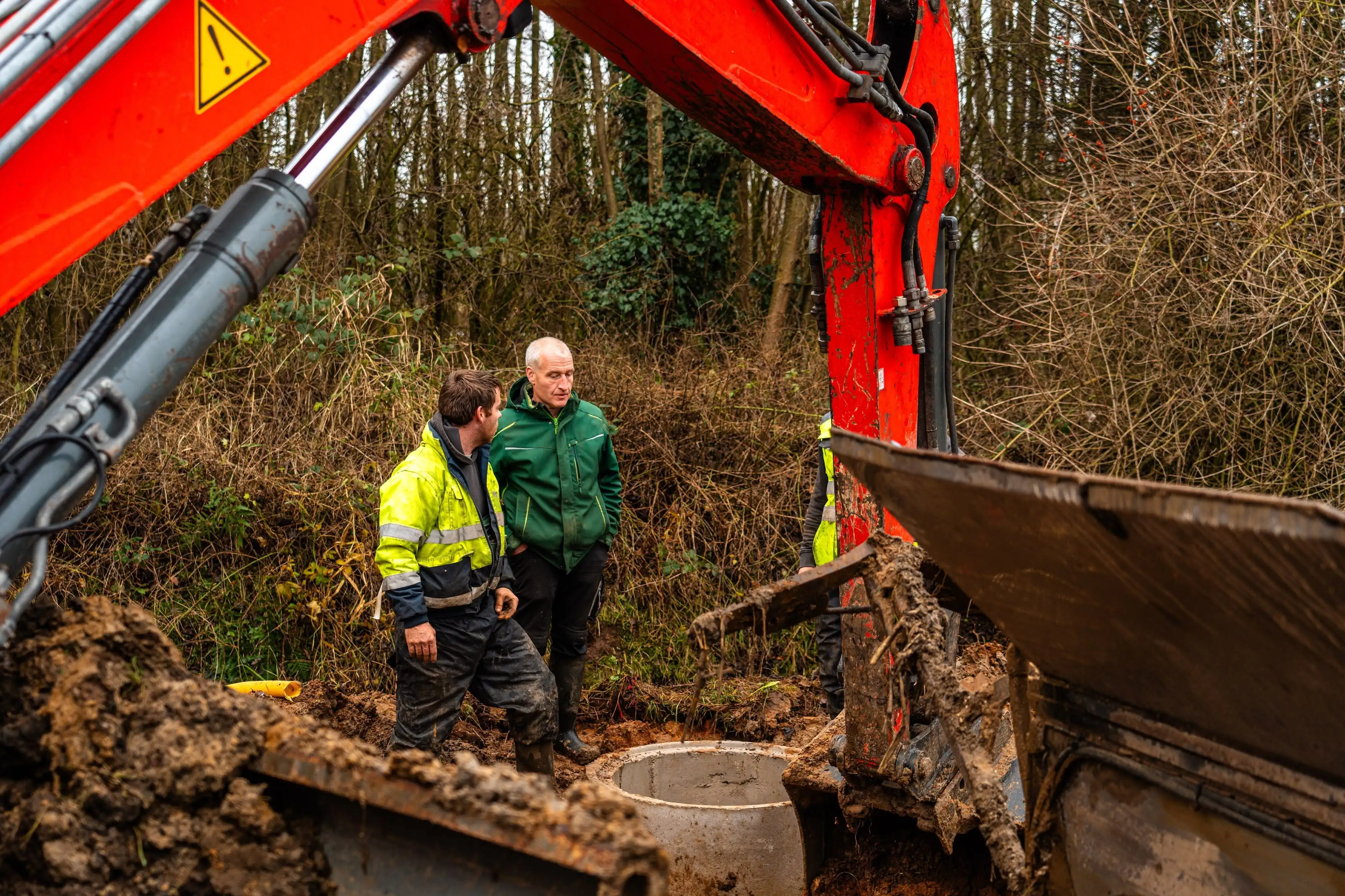 Two men standing in front of a large red excavator.