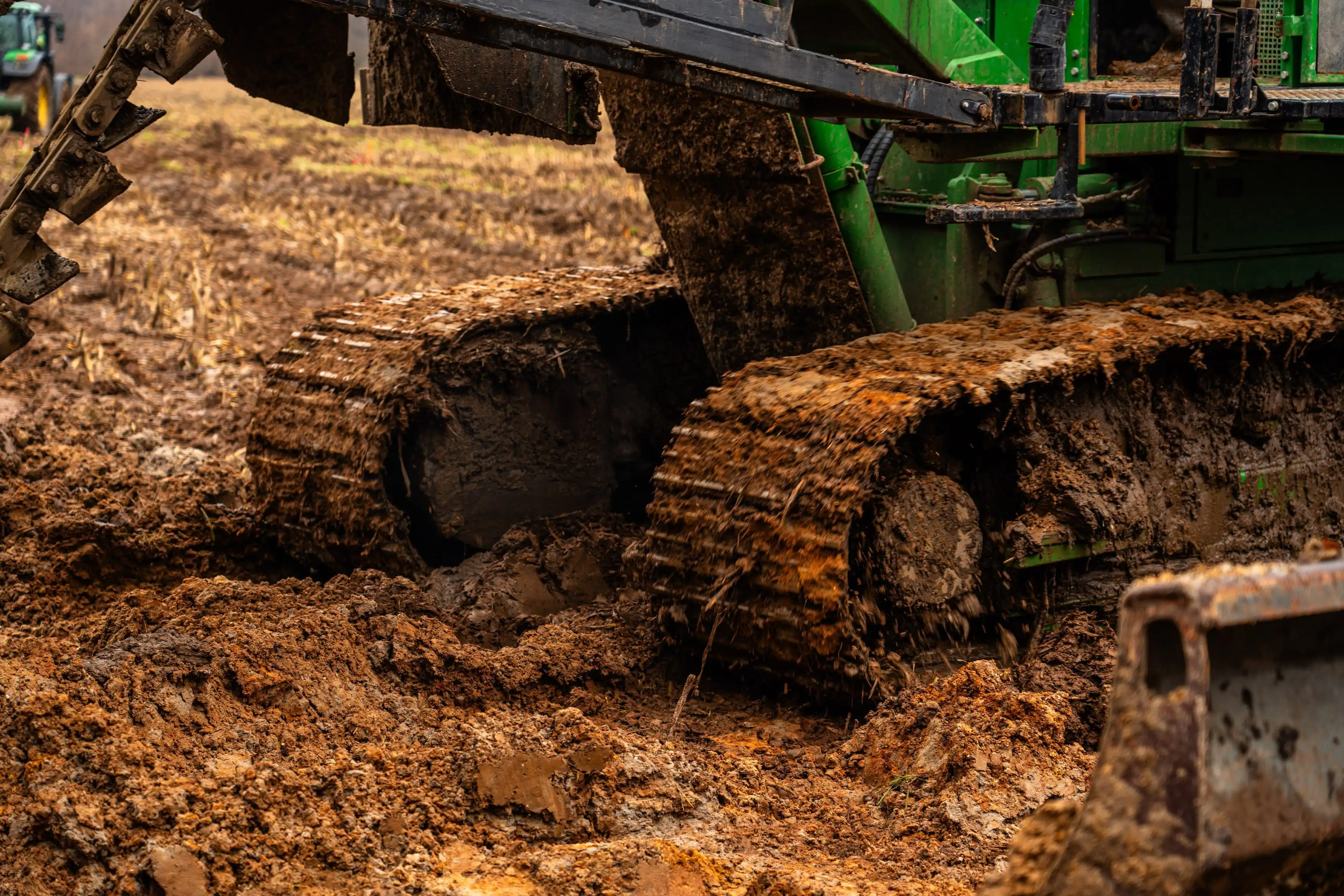 A green tractor with a large tire in the mud.