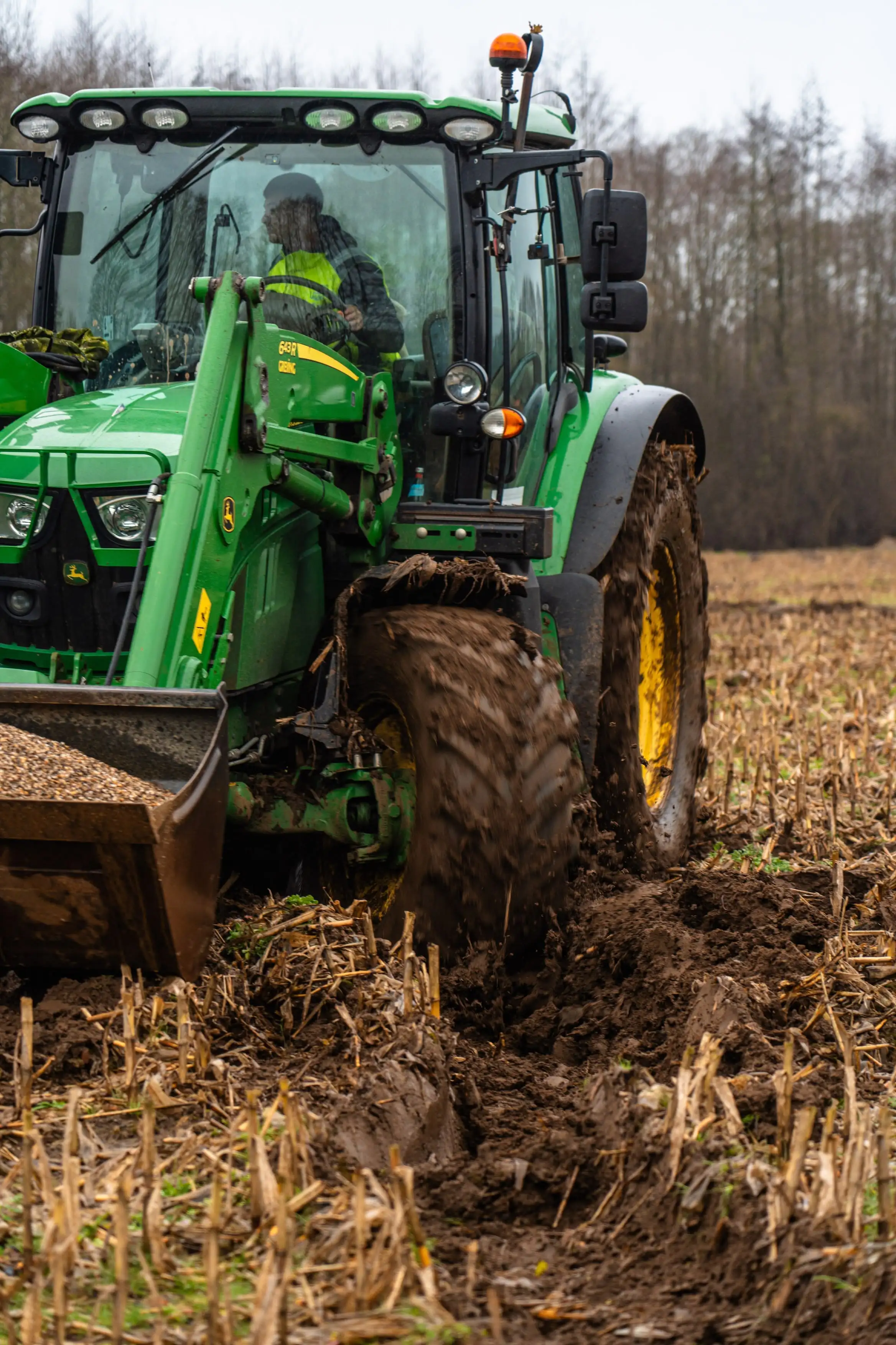 A green tractor with a yellow wheel and a man in a yellow vest driving it.