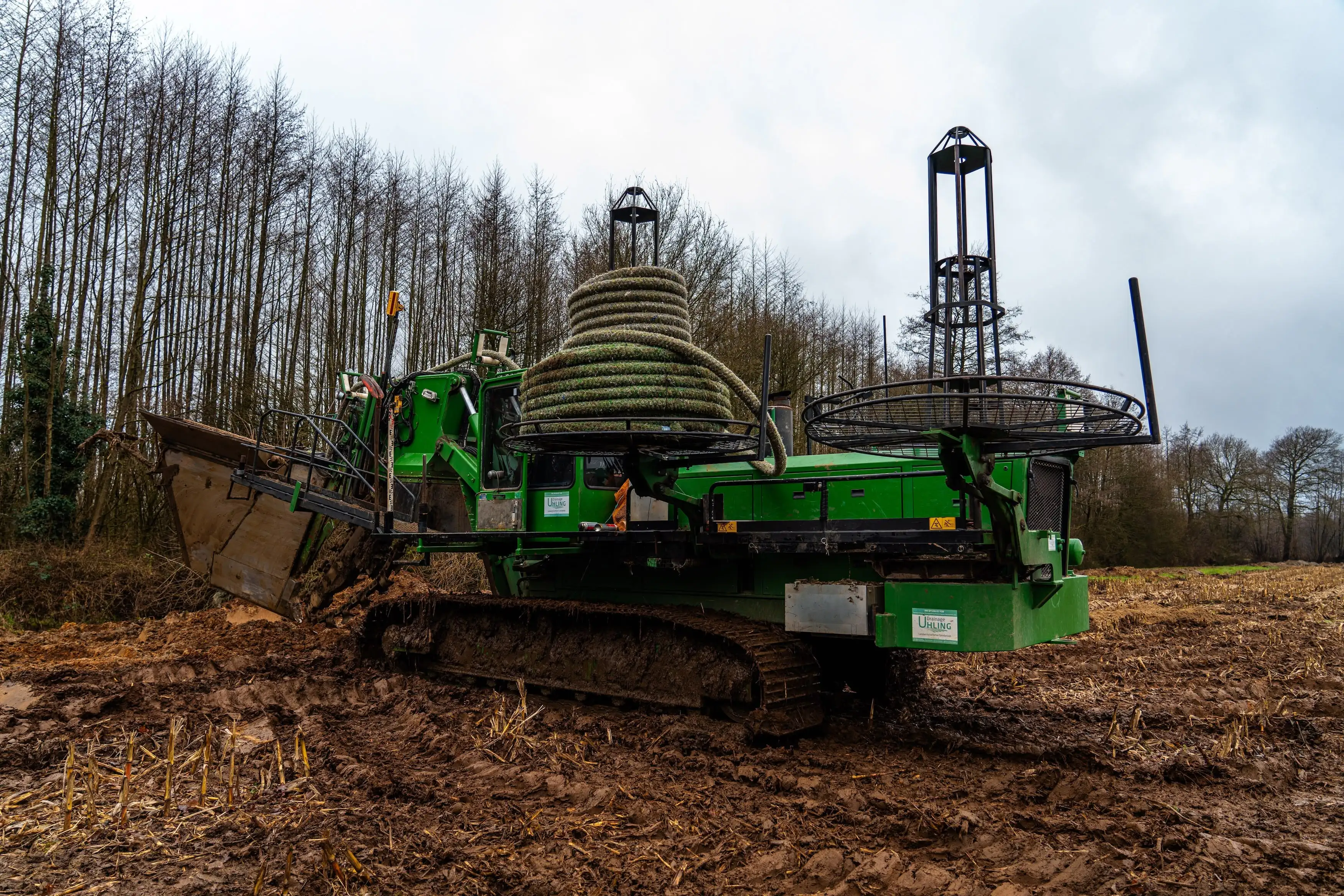 A large green machine is digging in the mud.