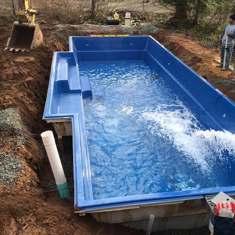 A man standing next to a blue swimming pool.