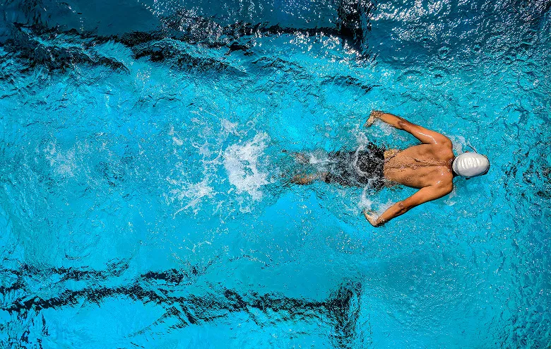 Swimmer in a white cap swimming in a pool, seen from above.