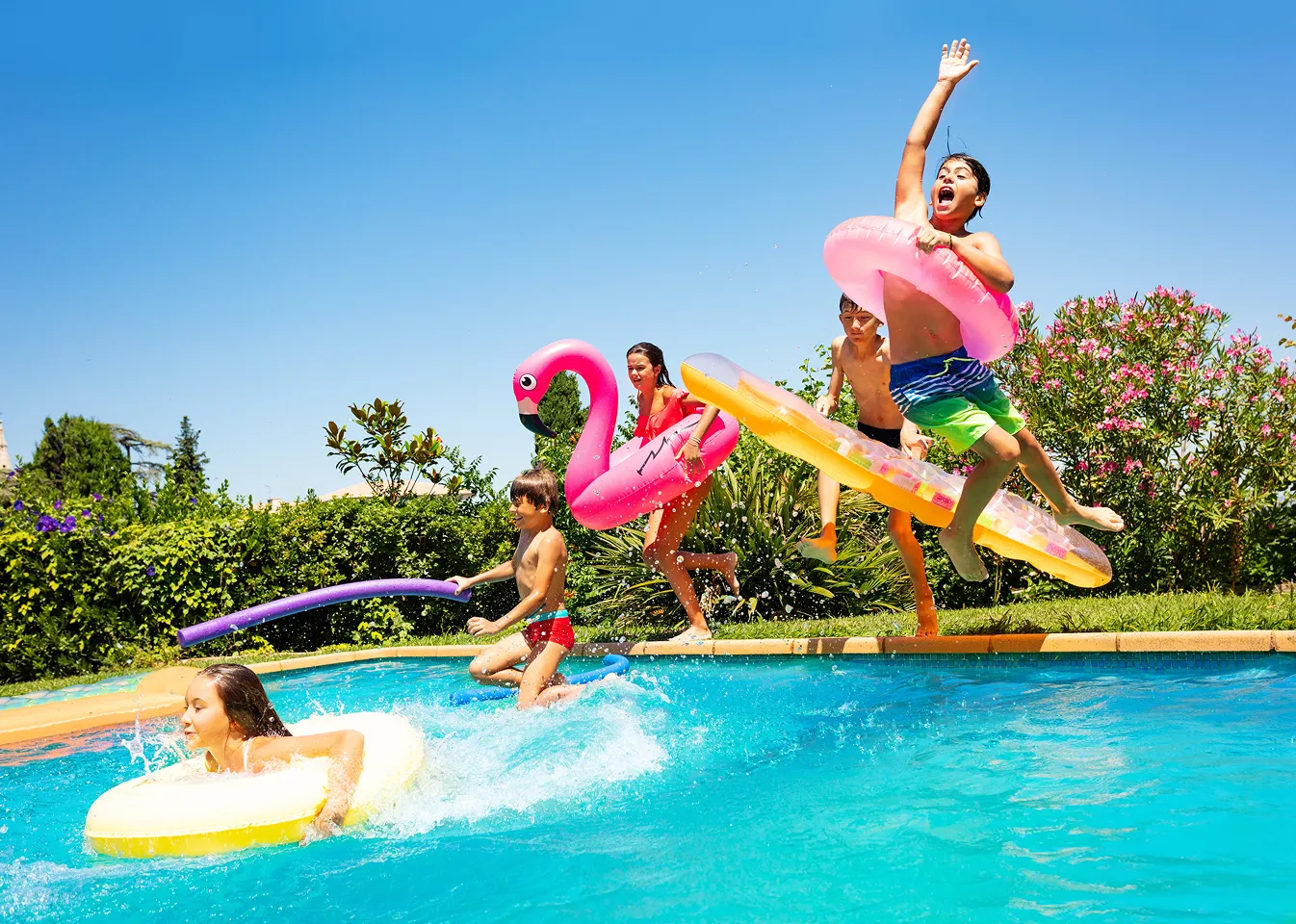 Five kids playing and jumping into a pool with colorful floaties on a sunny day