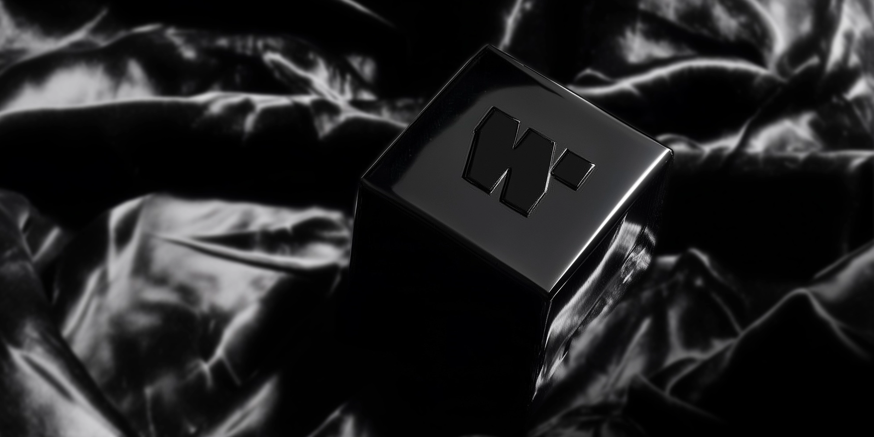 Black shiny cube with a raised 'W' logo placed on shiny black fabric.
