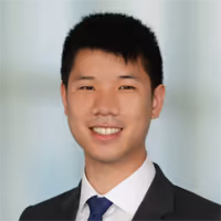 Portrait of an Asian-looking man in a grey suit, white shirt and blue tie smiling.