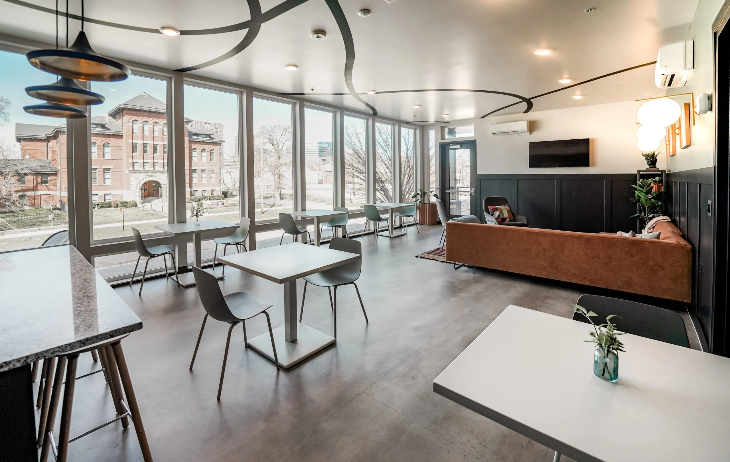 Interior view of the aQui355 apartment community lounge in Salt Lake City, UT, showcasing floor-to-ceiling windows, communal tables, and comfortable seating.