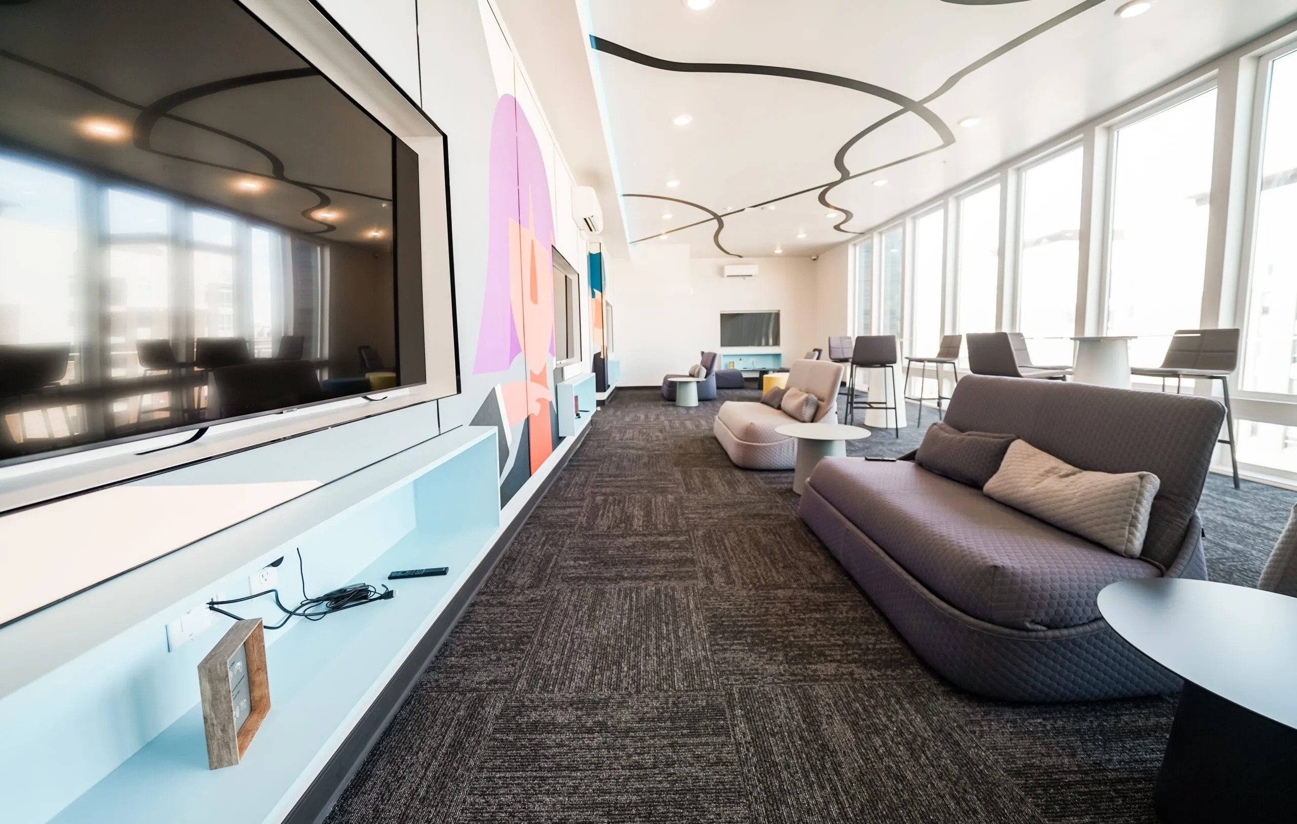 Lounge and media room at aQui355 apartments in Salt Lake City, UT, with a large TV, comfortable seating, and abstract wall art for resident enjoyment.