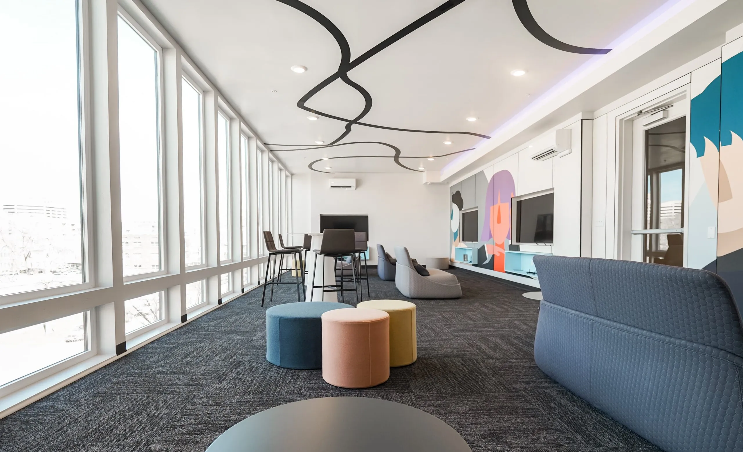 Vibrant resident lounge and media room at aQui355 apartments in Salt Lake City, Utah, with large screens, colorful murals, and various seating options.